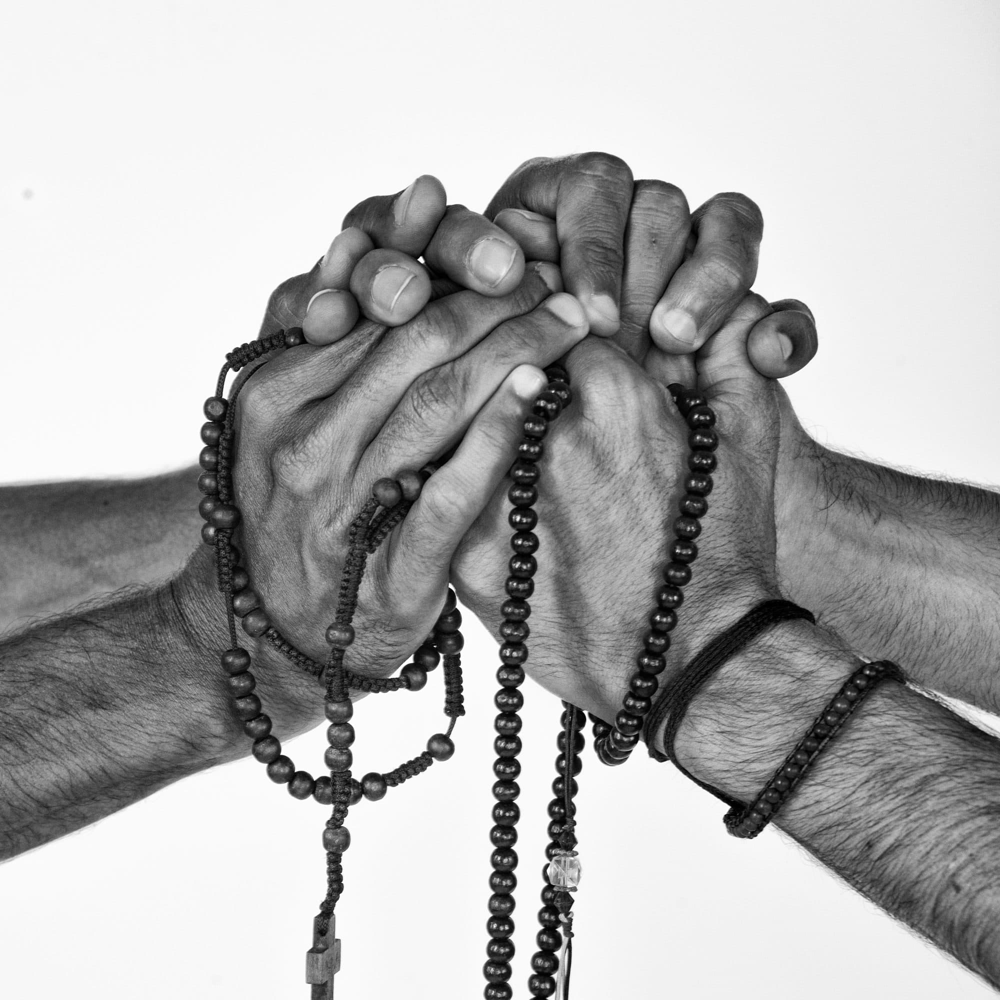 Hands of different strangers holding rosaries together