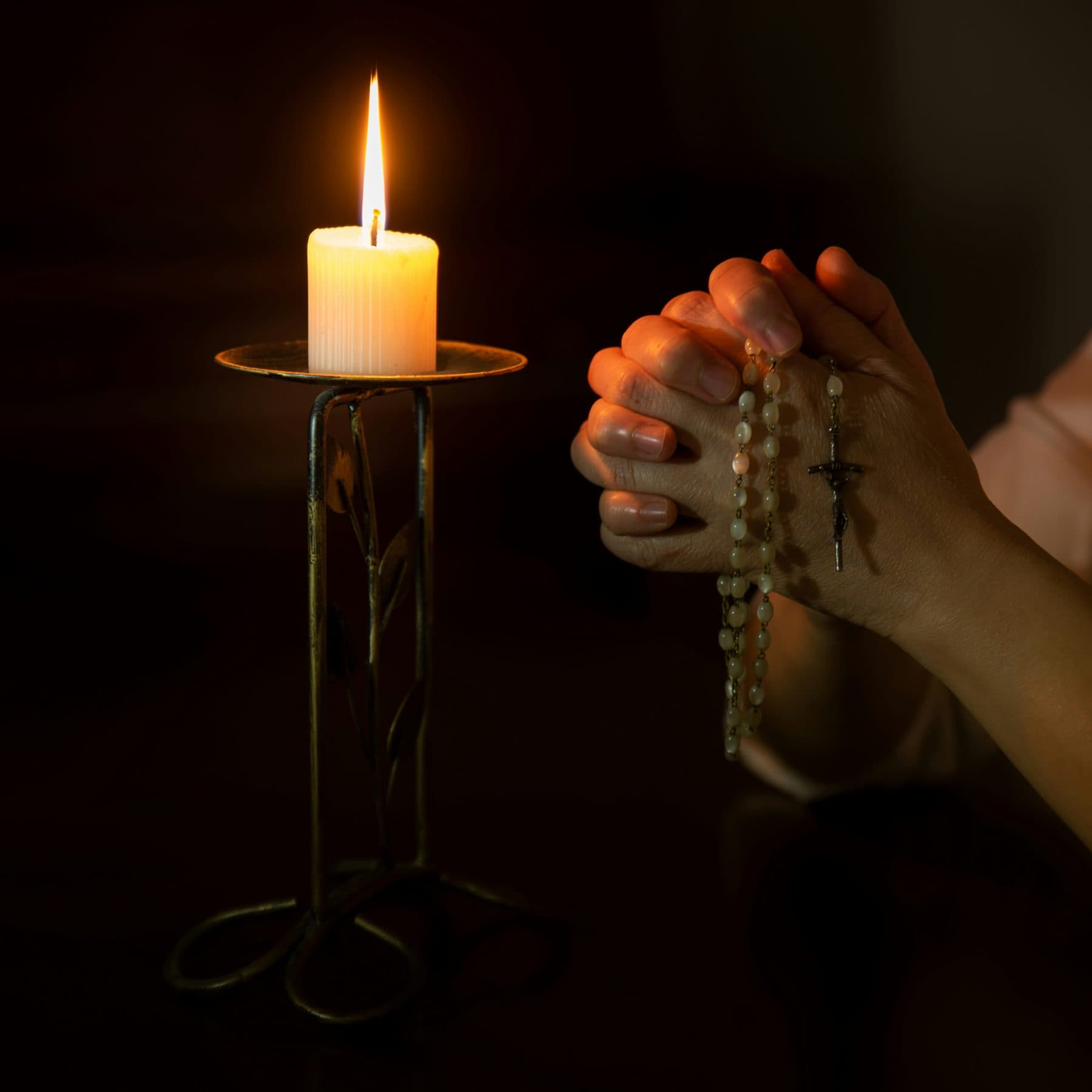 Hands holding a rosary beside a lit candle